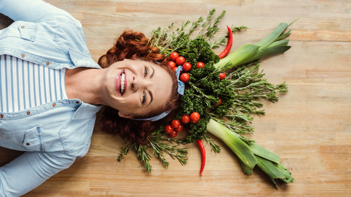 Lachende Frau mit Kräutern, Tomaten und Lauch als kreative Gemüsefrisur – steht für die Freude an bewusster Ernährung im Veganuary