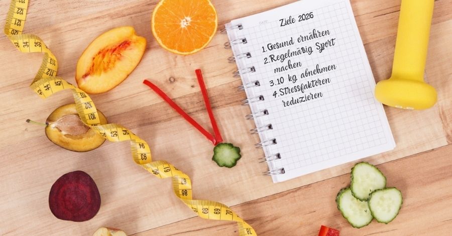 Ziele für 2026: Gesund ernähren, regelmäßig Sport machen, 10 kg abnehmen, Stress reduzieren – Notizbuch mit Obst, Maßband und Hantel auf einem Holztisch