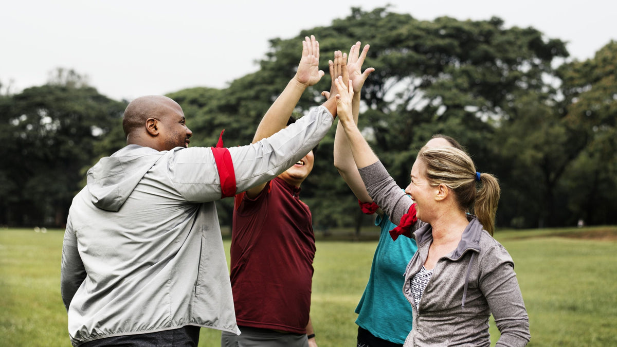 Gruppe aktiver Menschen gibt sich motiviert High Five im Park.
