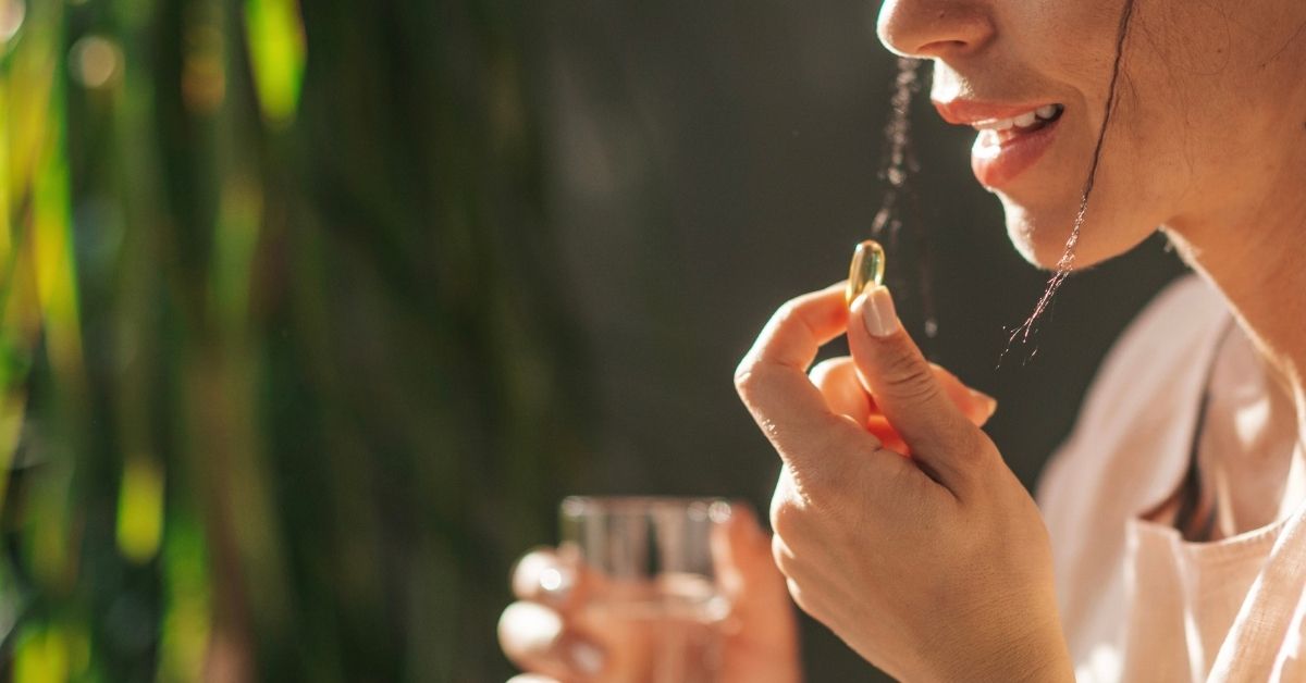 Frau nimmt eine Omega-3-Kapsel mit Wasser ein – veranschaulicht die einfache tägliche Omega-3-Dosierung im Alltag.